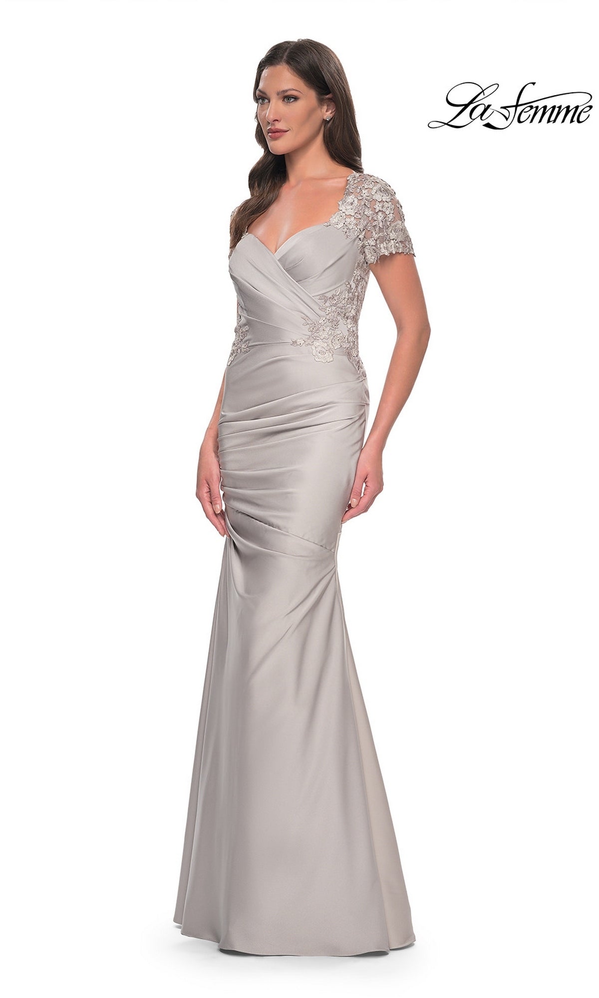 A woman wearing the La Femme 27989 long formal dress, featuring a fitted silver silhouette with lace applique short sleeves, a V-neckline, and ruched details. The La Femme logo is displayed in the top right corner.
