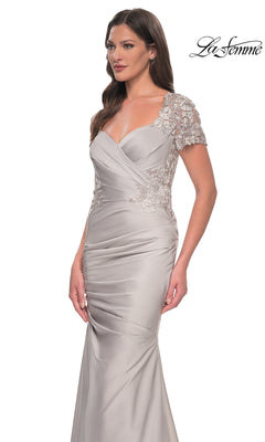 A woman models the Long Formal Dress: La Femme 27989, a fitted light gray gown with lace short sleeves and elegant floral applique accents in a graceful trumpet silhouette, standing against a white background with “La Femme” displayed in the top right corner.