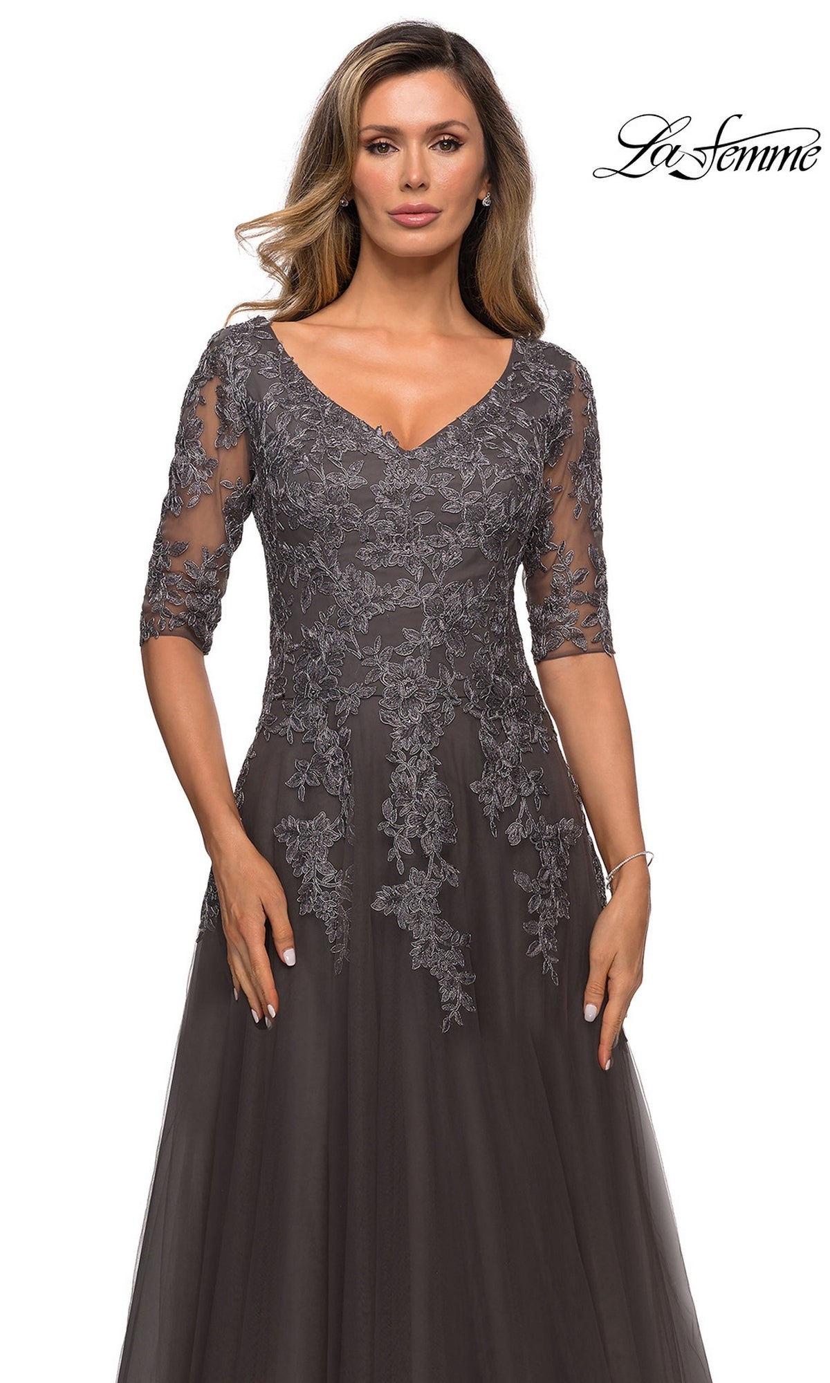 A woman wears a charcoal gray, A-line Long Formal Dress: La Femme 27993, featuring a V-neckline and three-quarter length sleeves with floral lace appliques.