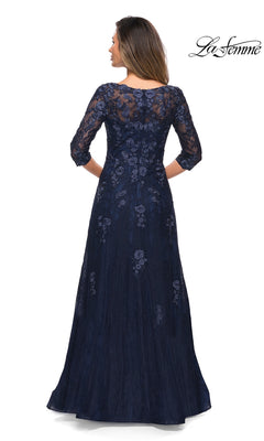 Woman in a floor-length navy blue lace Long Formal Dress: La Femme 28000 stands with her back to the camera; “La Femme” logo top right.