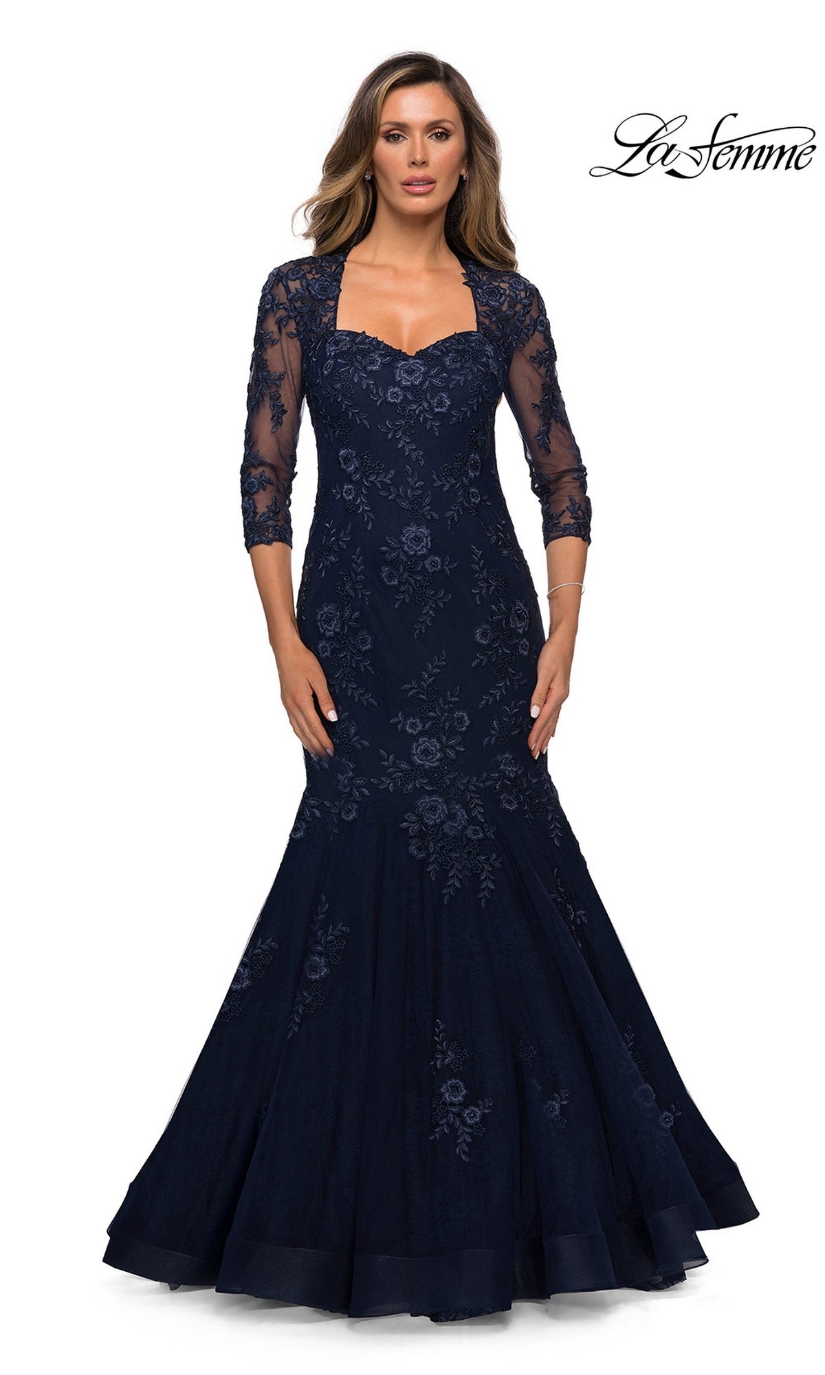 Woman in Long Formal Dress: La Femme 28033, navy mermaid style with floral lace and three-quarter sheer sleeves, standing against a white background.
