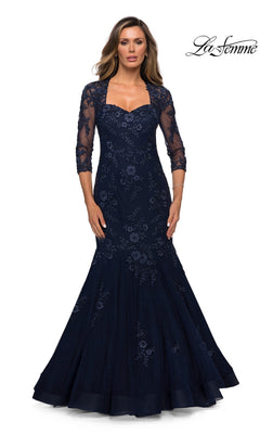 Woman in Long Formal Dress: La Femme 28033, navy mermaid style with floral lace and three-quarter sheer sleeves, standing against a white background.