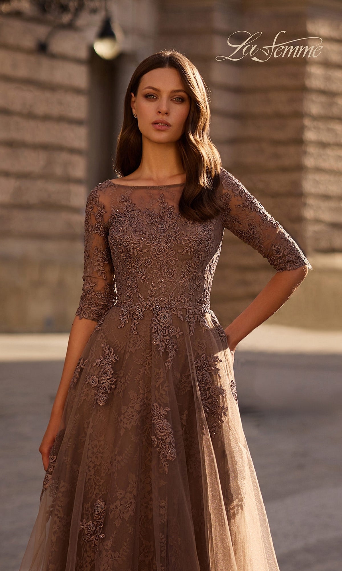 Woman outdoors in the Long Formal Dress: La Femme 28036 with tulle A-line skirt, three-quarter sleeves, and floral lace embroidery, looking at the camera.