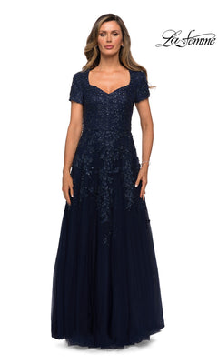 A woman wears a navy La Femme 28037 floor-length A-line gown featuring a sweetheart neckline, short sleeves, and a bodice with sequined floral appliqué.