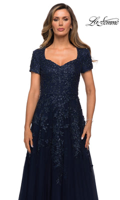A woman wears a navy blue Long Formal Dress: La Femme 28037 featuring a sweetheart neckline, short sleeves, and intricate beaded appliques on the bodice over an A-line tulle skirt.