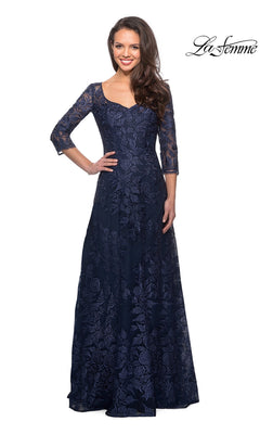 Woman wearing Long Formal Dress: La Femme 28053 in navy, floor-length lace with three-quarter sleeves, smiling against a white background. “La Femme” logo in top right corner.