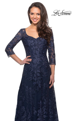 Smiling woman in Long Formal Dress: La Femme 28053, a navy blue three-quarter sleeve lace dress with floral patterns, against a white background.