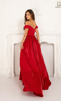 A woman in the Lucci Lu 28063 off-the-shoulder satin prom dress stands before a white ornate fireplace, gazing over her shoulder.
