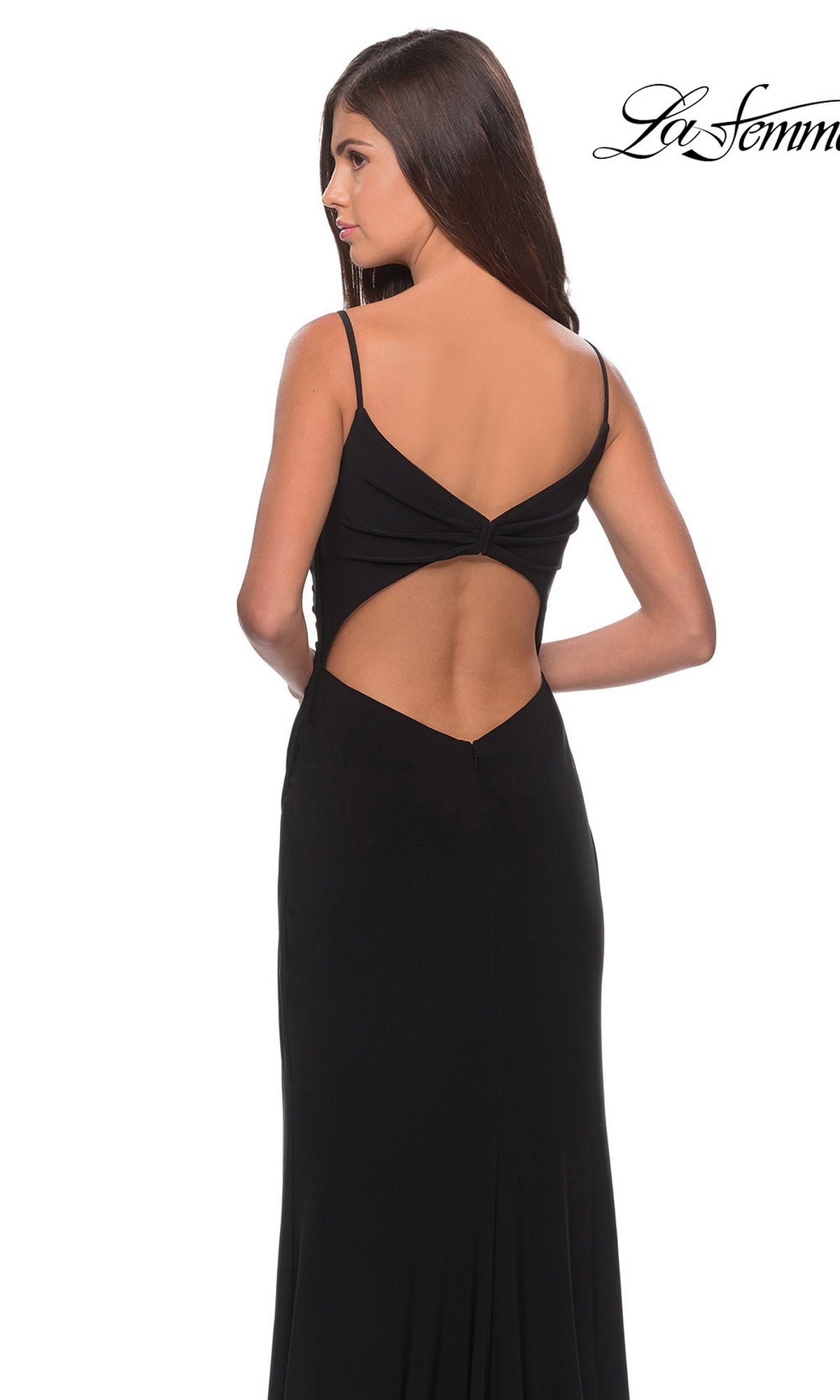 A woman with long brown hair is wearing the La Femme 28079 long prom dress—a sleeveless black jersey gown with a low back, faux wrap design, chic cut-out detail, and a striking thigh-high slit—standing against a white background.