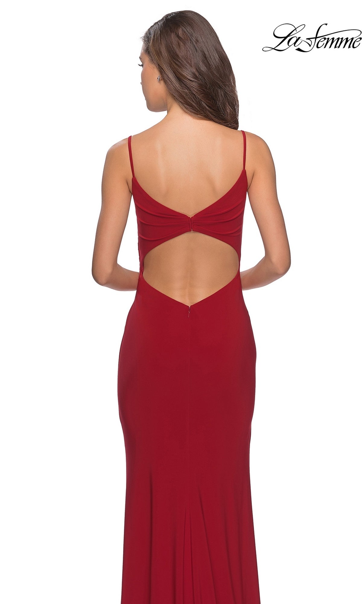 A woman faces away from the camera wearing the La Femme 28079 long prom dress—a red, backless evening gown with thin straps, a subtle faux wrap design, and a daring thigh-high leg slit. The “La Femme” brand logo appears in the top right corner.