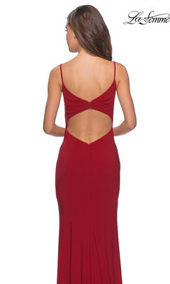 A woman faces away from the camera wearing the La Femme 28079 long prom dress—a red, backless evening gown with thin straps, a subtle faux wrap design, and a daring thigh-high leg slit. The “La Femme” brand logo appears in the top right corner.