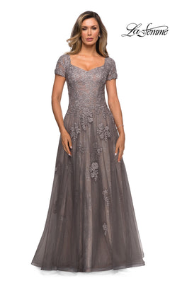 A woman wears a platinum Long Formal Dress: La Femme 28091 featuring a floor-length silhouette, short lace sleeves, a sweetheart neckline, and floral embroidery.