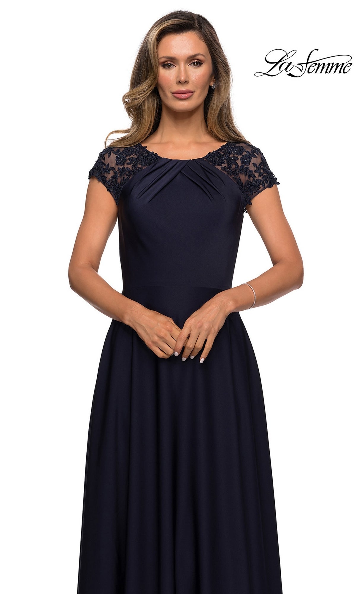 A woman standing against a white background wears the La Femme 28100 long formal dress, a navy blue A-line gown featuring lace cap sleeves and a pleated bodice. The La Femme logo appears in the upper right corner.