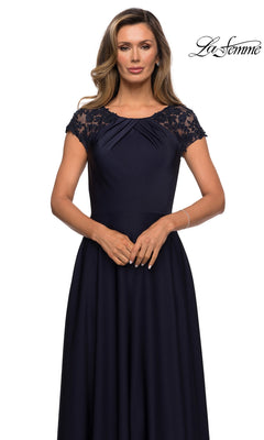 A woman standing against a white background wears the La Femme 28100 long formal dress, a navy blue A-line gown featuring lace cap sleeves and a pleated bodice. The La Femme logo appears in the upper right corner.