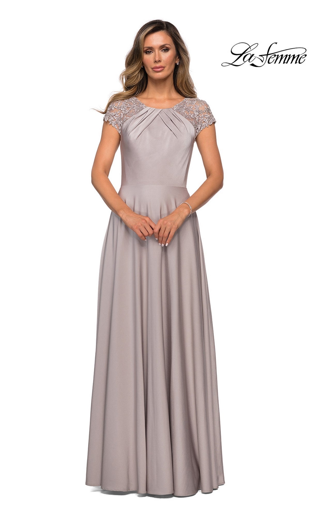 A woman wears a floor-length, short-sleeved, silver modest dress (La Femme 28100) featuring lace detailing on the shoulders and an elegant A-line silhouette, standing against a white background. The “La Femme” logo appears in the top right corner.