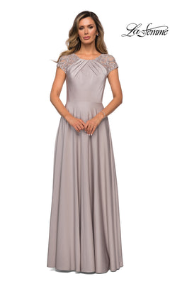 A woman wears a floor-length, short-sleeved, silver modest dress (La Femme 28100) featuring lace detailing on the shoulders and an elegant A-line silhouette, standing against a white background. The “La Femme” logo appears in the top right corner.
