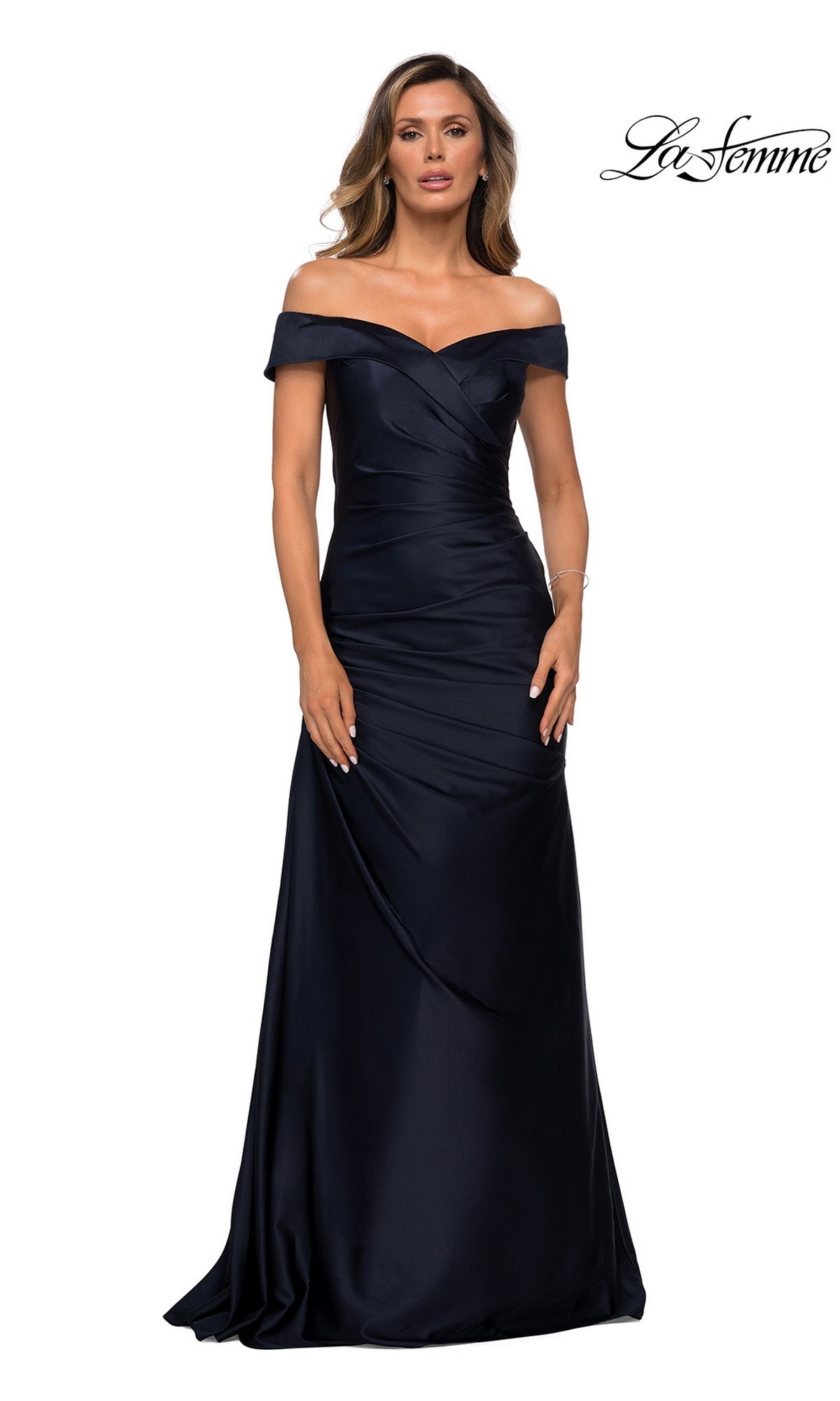 A woman wears the La Femme 28103 long formal dress in navy, featuring an off-the-shoulder neckline, floor-length fitted silhouette, and subtle pleating, standing against a white background. Ideal as a satin mother-of-the-bride gown. The “La Femme” logo appears in the top right corner.