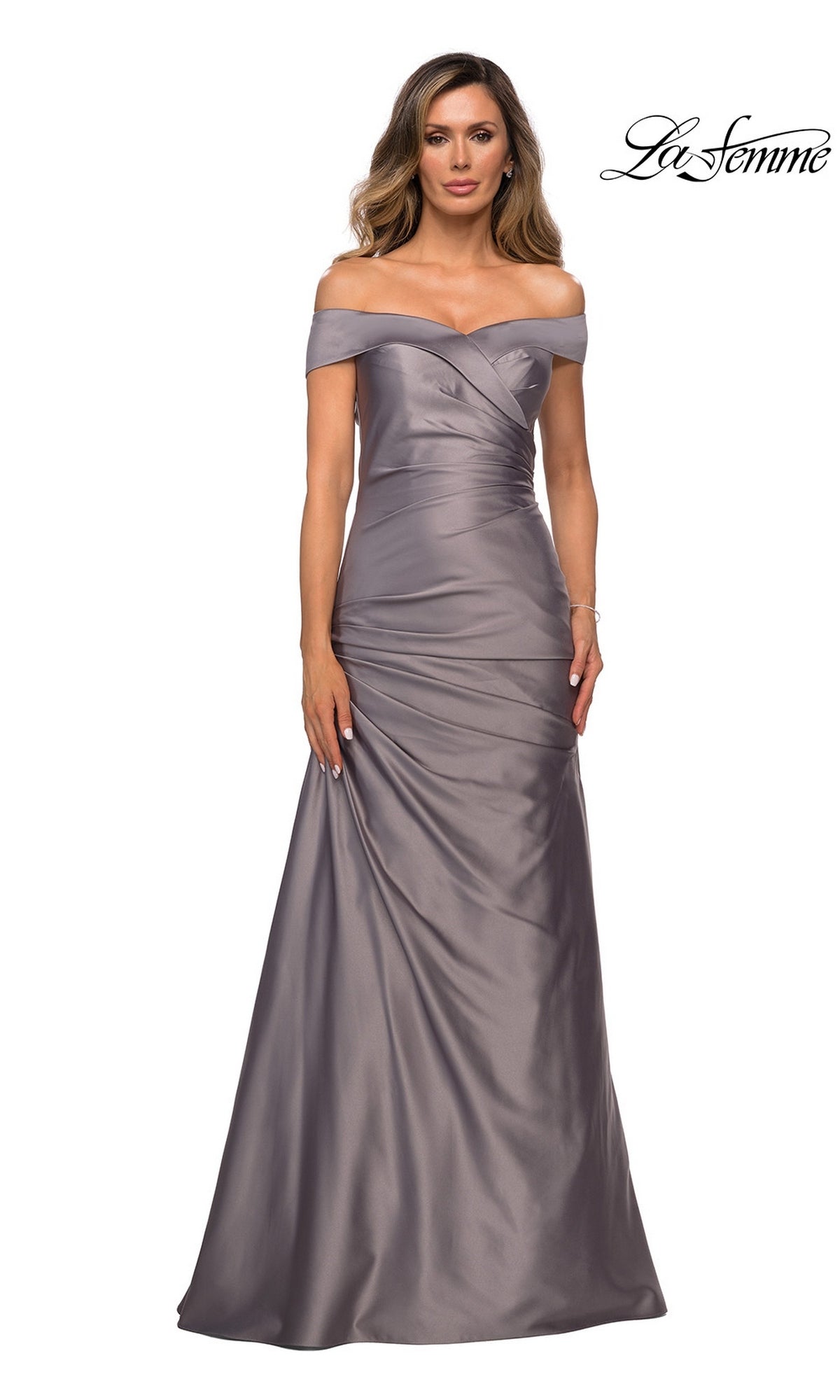 A woman wears the La Femme 28103, a platinum, off-the-shoulder, floor-length satin formal dress featuring ruched detailing; the “La Femme” logo appears in the top right corner—perfect for an elegant mother-of-the-bride look.