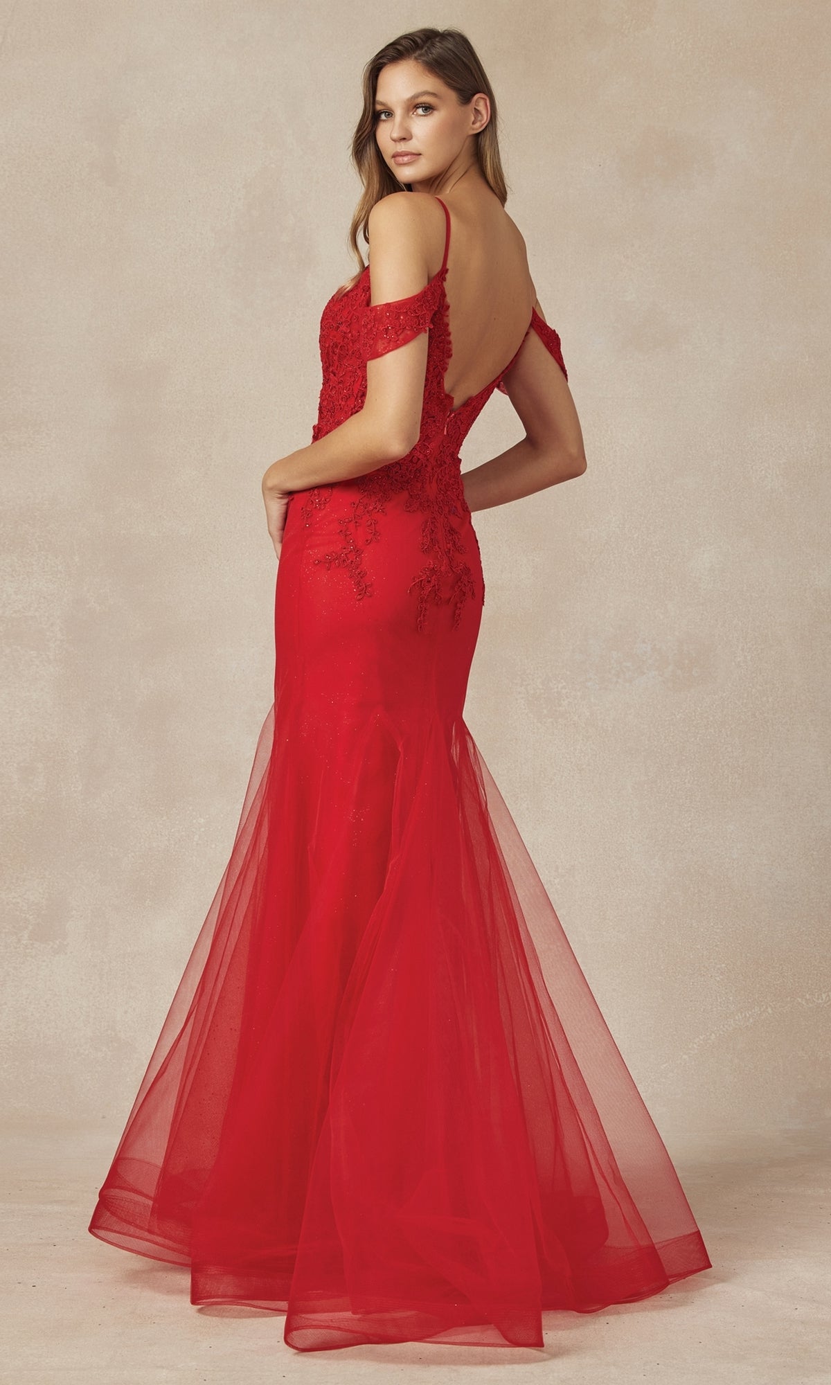 A woman in the Long Glitter Mermaid Prom Dress: Juliet 281, featuring a floor-length silhouette, off-the-shoulder style, lace detailing, and a low back, stands turned slightly away from the camera.