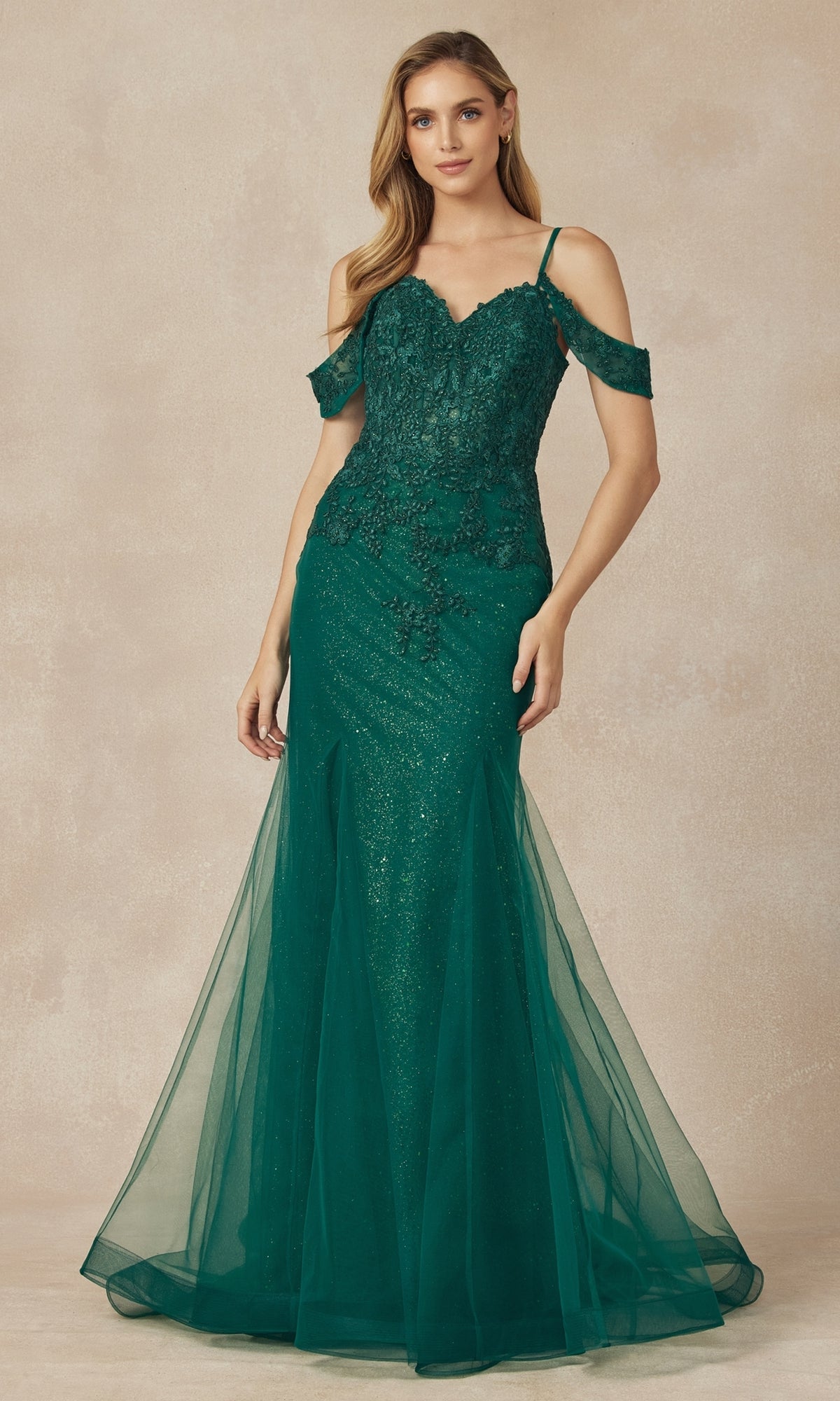 A woman wearing the Juliet 281 Long Glitter Mermaid Prom Dress, featuring an off-the-shoulder floor-length design in emerald green with lace and tulle, stands against a neutral background.
