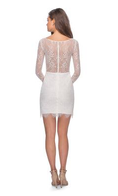 A woman faces away, wearing the La Femme Short White Rehearsal-Dinner Dress 28233 with long sleeves and floral lace, paired with nude high-heeled sandals, against a plain white background.