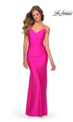 A woman wears the La Femme Backless Long V-Neck Prom Dress 28287, a fitted, floor-length bright pink gown with thin straps and a backless design, standing against a plain white background. The "La Femme" logo appears in the top right corner.