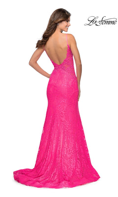 A woman models the La Femme Backless Long Lace Prom Dress 28355 in bright pink, featuring a mermaid skirt, low back, and thin straps as she stands facing away from the camera.