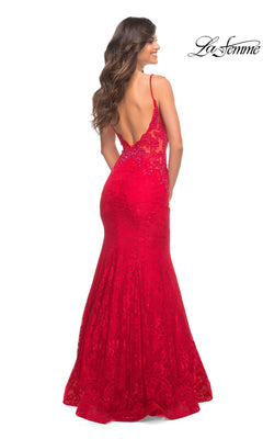 A woman models the La Femme Backless Long Lace Prom Dress 28355—a fitted, floor-length red lace gown with a mermaid skirt and open back—standing against a white background.