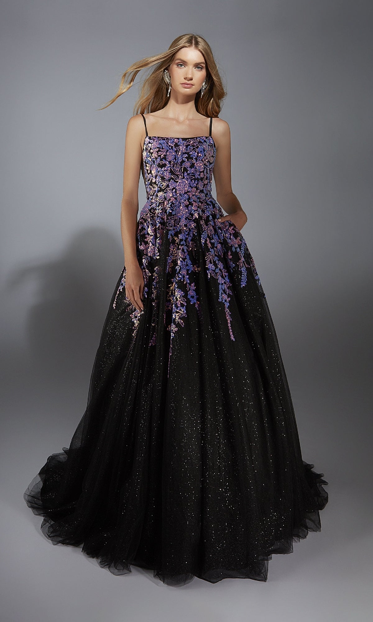 A woman in the Aerie Couture 283 long formal dress, featuring thin straps and embellished floral details, poses against a plain gray background.