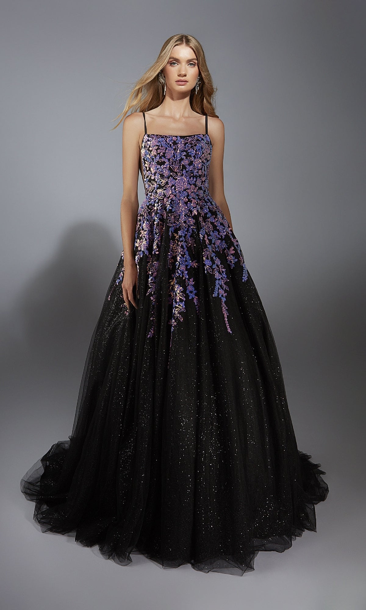 A woman poses against a plain gray background wearing the Long Formal Dress: Aerie Couture 283, featuring an a-line glitter tulle skirt, floral embellishments, and thin straps.