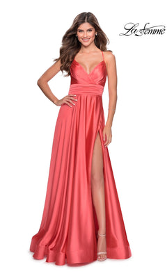 A woman in the La Femme Banded-Waist Long A-Line Prom Dress 28571, a sleeveless coral pink satin gown with a thigh-high slit, stands smiling. The "La Femme" logo appears in the top right corner.