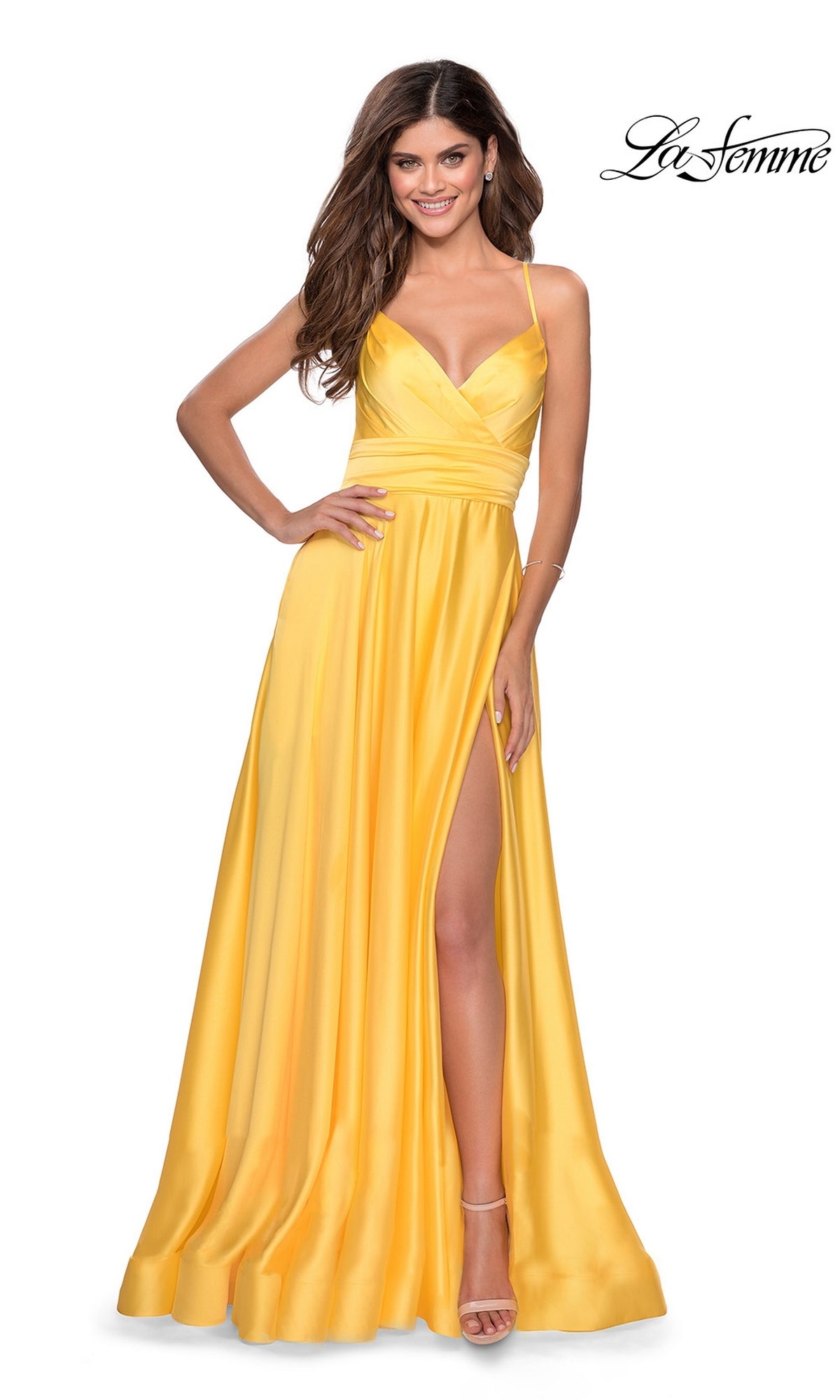 A woman in the La Femme Banded-Waist Long A-Line Prom Dress 28571—a yellow sleeveless gown with thigh-high slit and spaghetti straps—smiles while wearing strappy heels. 