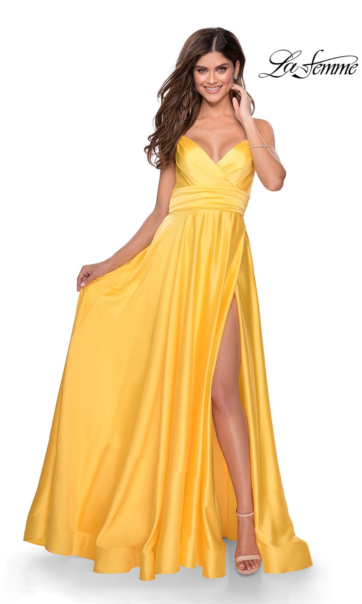 A woman stands in a sleeveless yellow La Femme Banded-Waist Long A-Line Prom Dress 28571 with a high slit, holding out one side of the gown; the 