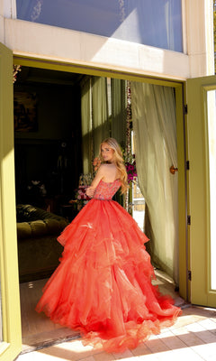 A woman in a one-shoulder Ava Presley 28575 prom ball gown stands in an open doorway, glancing back over her shoulder at the camera.