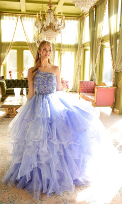 A woman stands in a sunlit room wearing the Ava Presley 28575 one-shoulder prom ball gown, surrounded by elegant furniture and chandeliers.