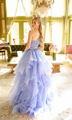 A woman in the Ava Presley 28575 one-shoulder prom ball gown stands in a chic, sunlit room adorned with chandeliers, green walls, and vintage furniture.