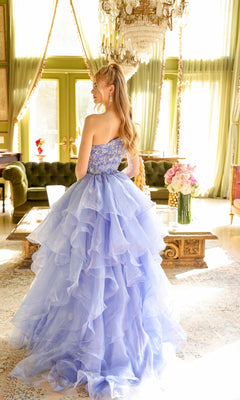 A woman in the One-Shoulder Prom Ball Gown: Ava Presley 28575 stands in an elegant, sunlit room with green walls, chandeliers, and large windows.