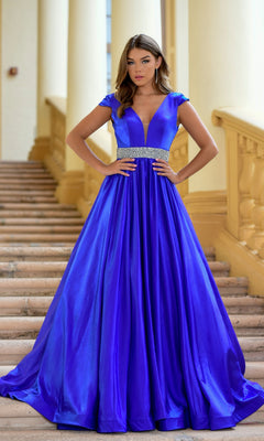 A woman stands on stairs wearing the Long Formal Dress 28580 by Ava Presley, featuring cap sleeves, a deep V-neckline, a jeweled waistband, and royal blue color.