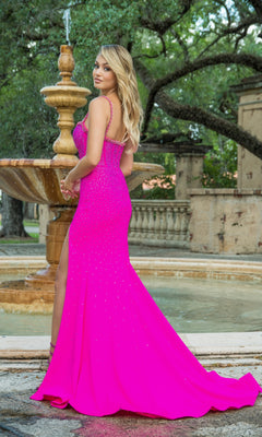 A woman wears the Ava Presley Long Formal Dress 28581 in bright pink, featuring a corset bodice, as she stands before a stone fountain in an outdoor garden.