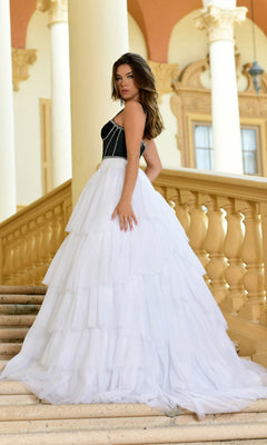 A woman stands on an outdoor staircase in the Long Formal Dress 28592 by Ava Presley, a black and white ball gown with an elegant A-line skirt, framed by columns and ornate architecture in the background.