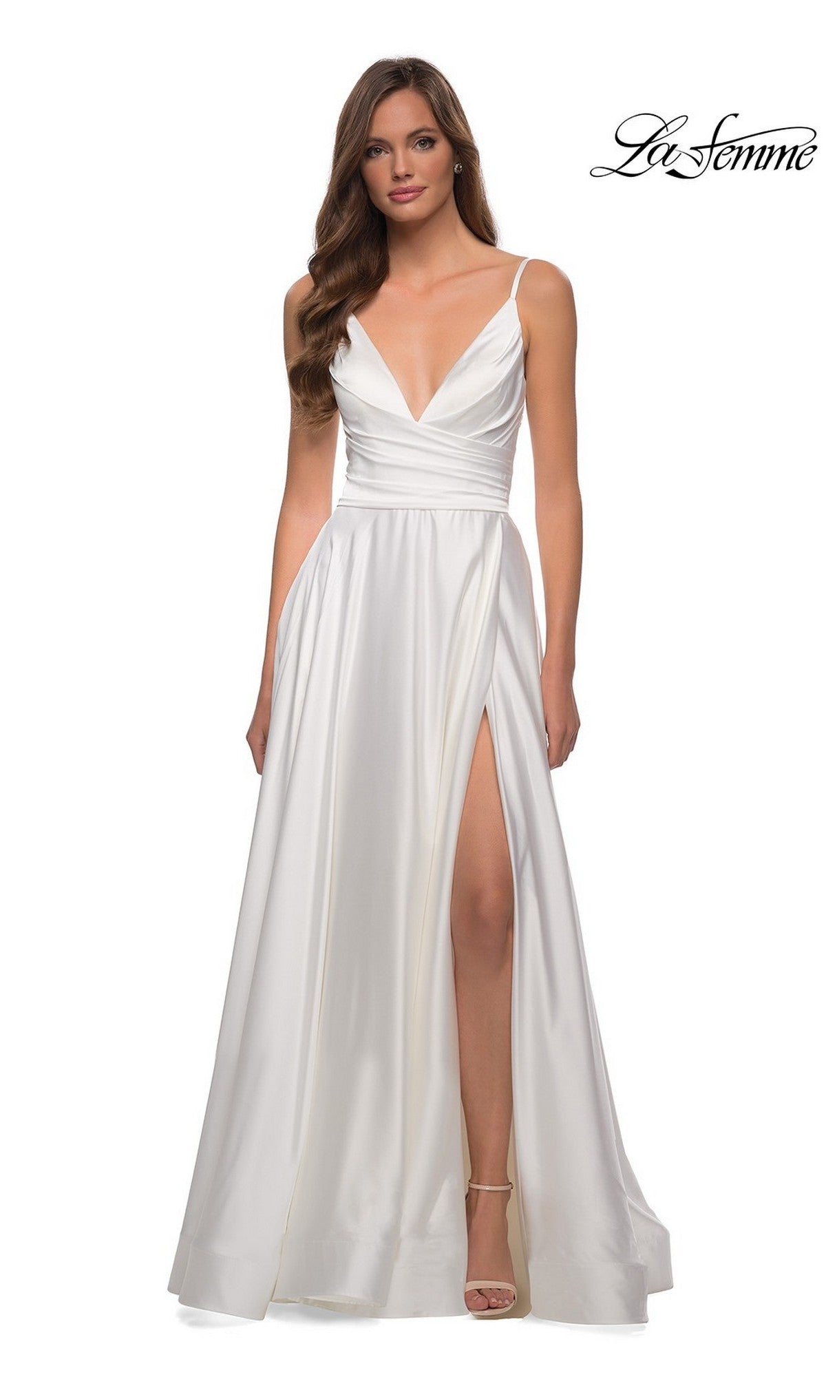 A woman wears the La Femme V-Neck Long A-Line Prom Dress 28607, a white satin gown with thin straps, deep V-neckline, and high front slit. She stands against a plain background with the La Femme logo at the top right corner.