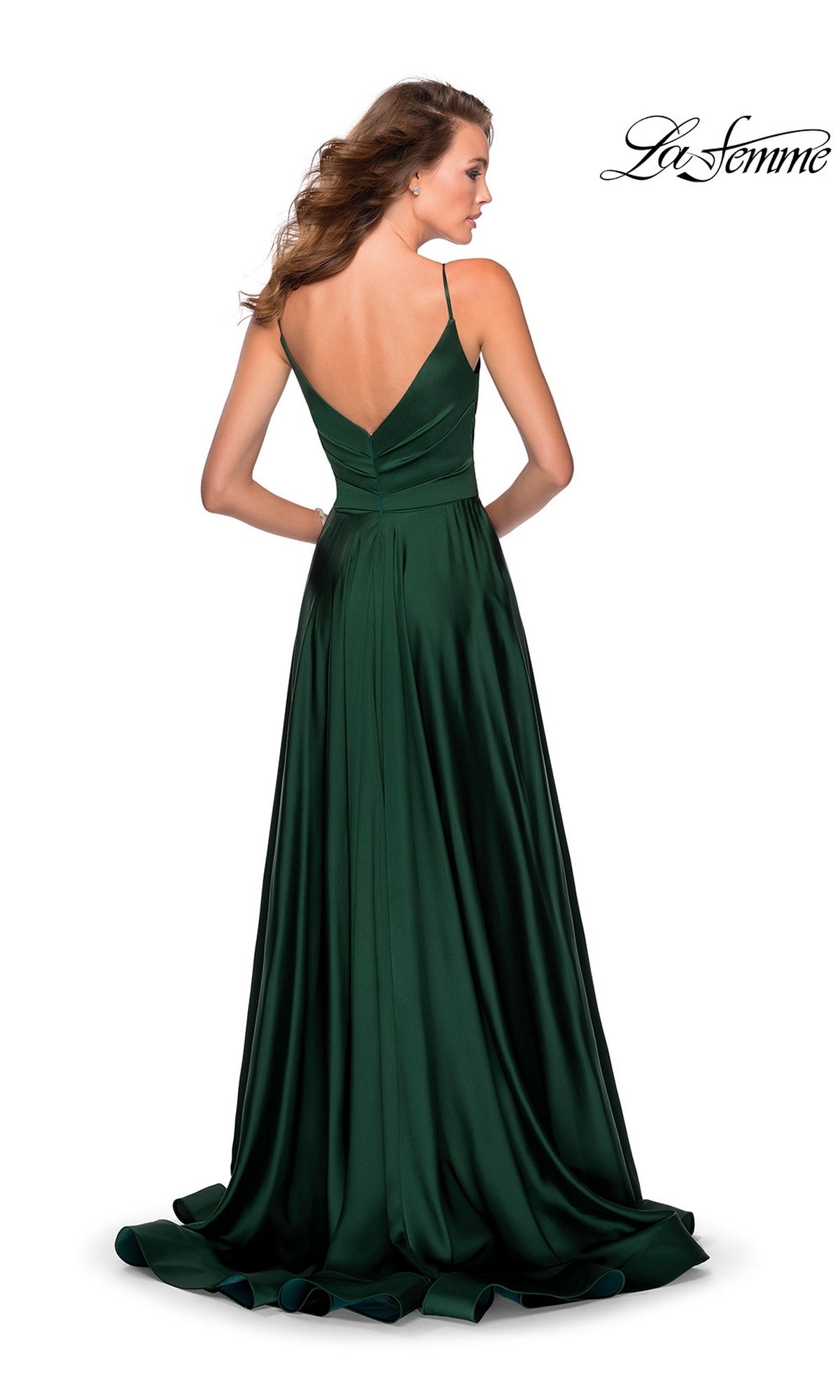 Woman in a La Femme V-Neck Long A-Line Prom Dress 28607, floor-length dark green satin with thin straps and a V-shaped back, standing and facing away from the camera. This gown embodies classic sophistication.