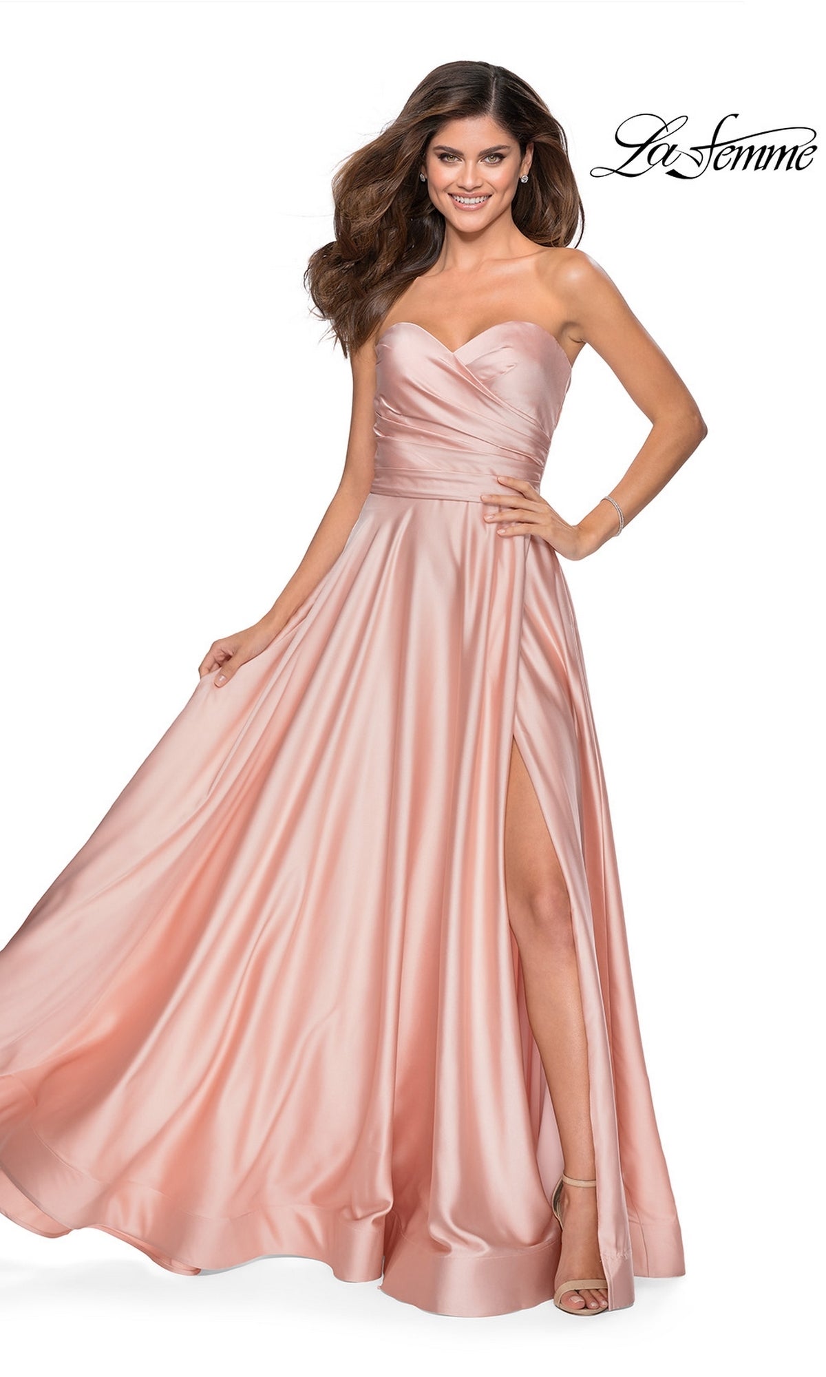 Woman in the La Femme Strapless Long A-Line Prom Dress 28608, featuring a blush pink satin fabric, strapless sweetheart neckline, and high slit, stands smiling.