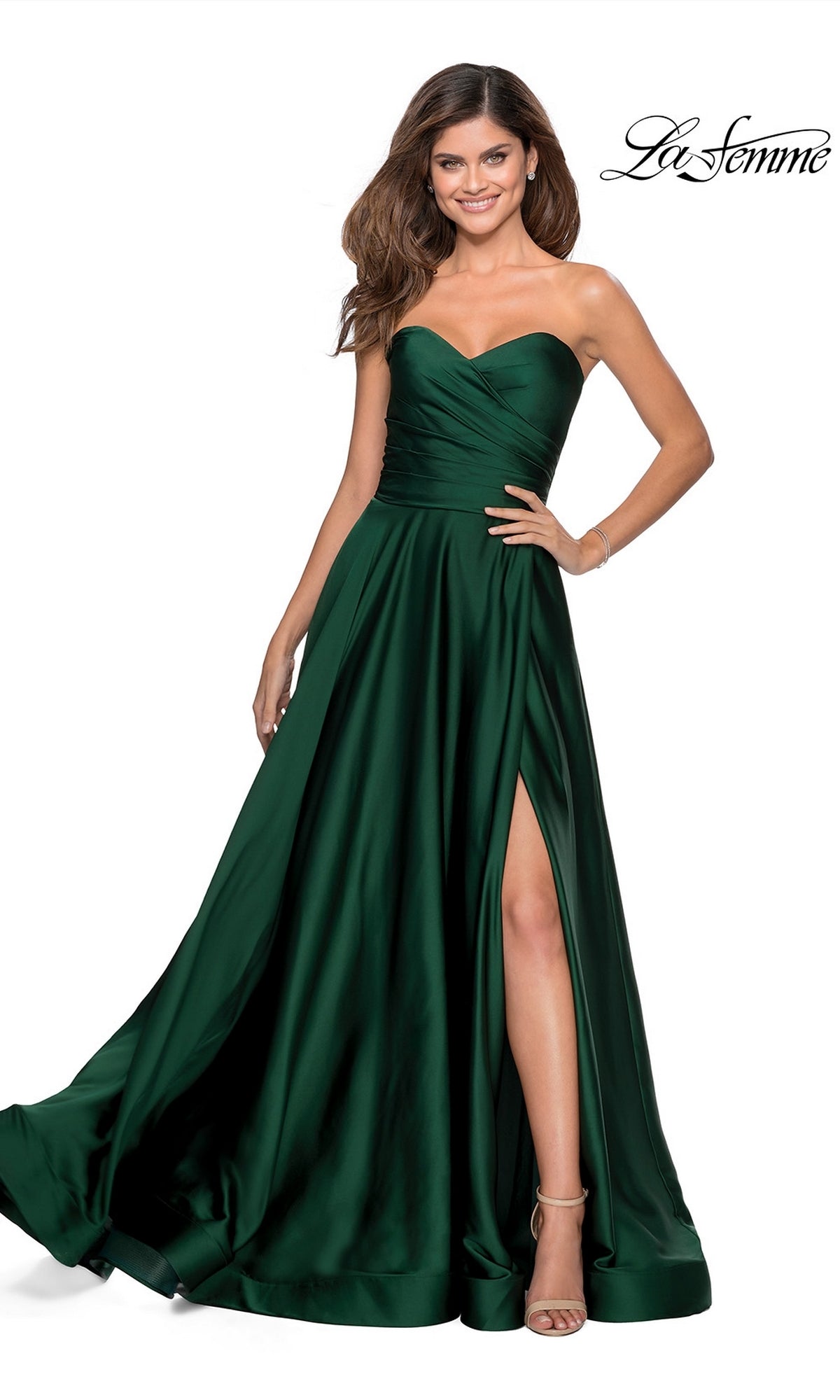 A woman wearing a La Femme Strapless Long A-Line Prom Dress 28608 stands and smiles. The dark green satin gown features a strapless sweetheart neckline and a high leg slit.