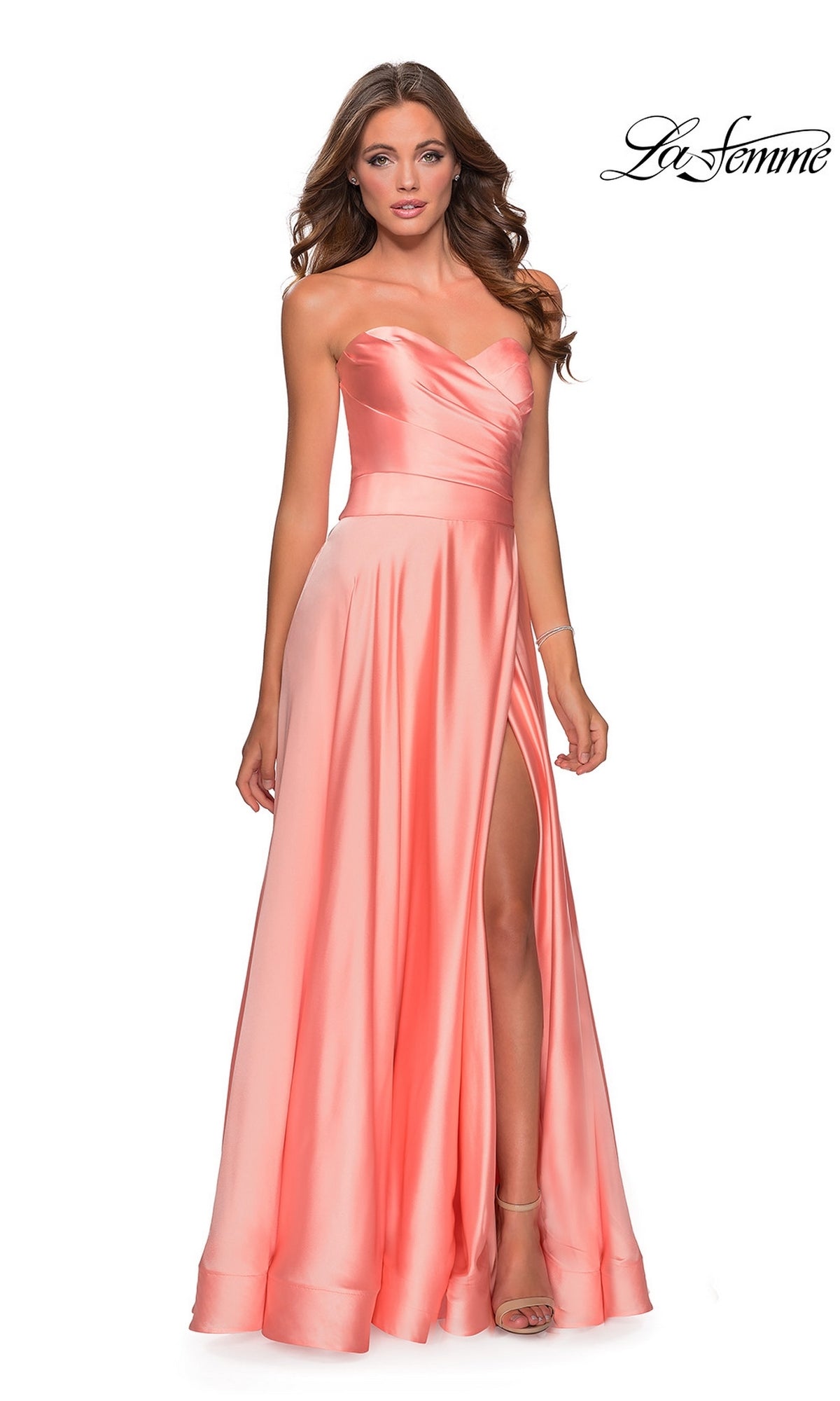A woman in the La Femme Strapless Long A-Line Prom Dress 28608, featuring a coral satin strapless sweetheart neckline and side slit, stands against a white background with the 