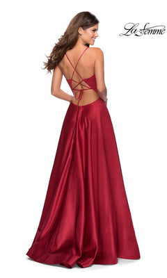 A woman models the La Femme Strappy-Back Long A-Line Prom Dress 28628, a red satin gown with a v-neck, crisscross open back, and flowing skirt, smiling over her shoulder in this stunning formal dress.