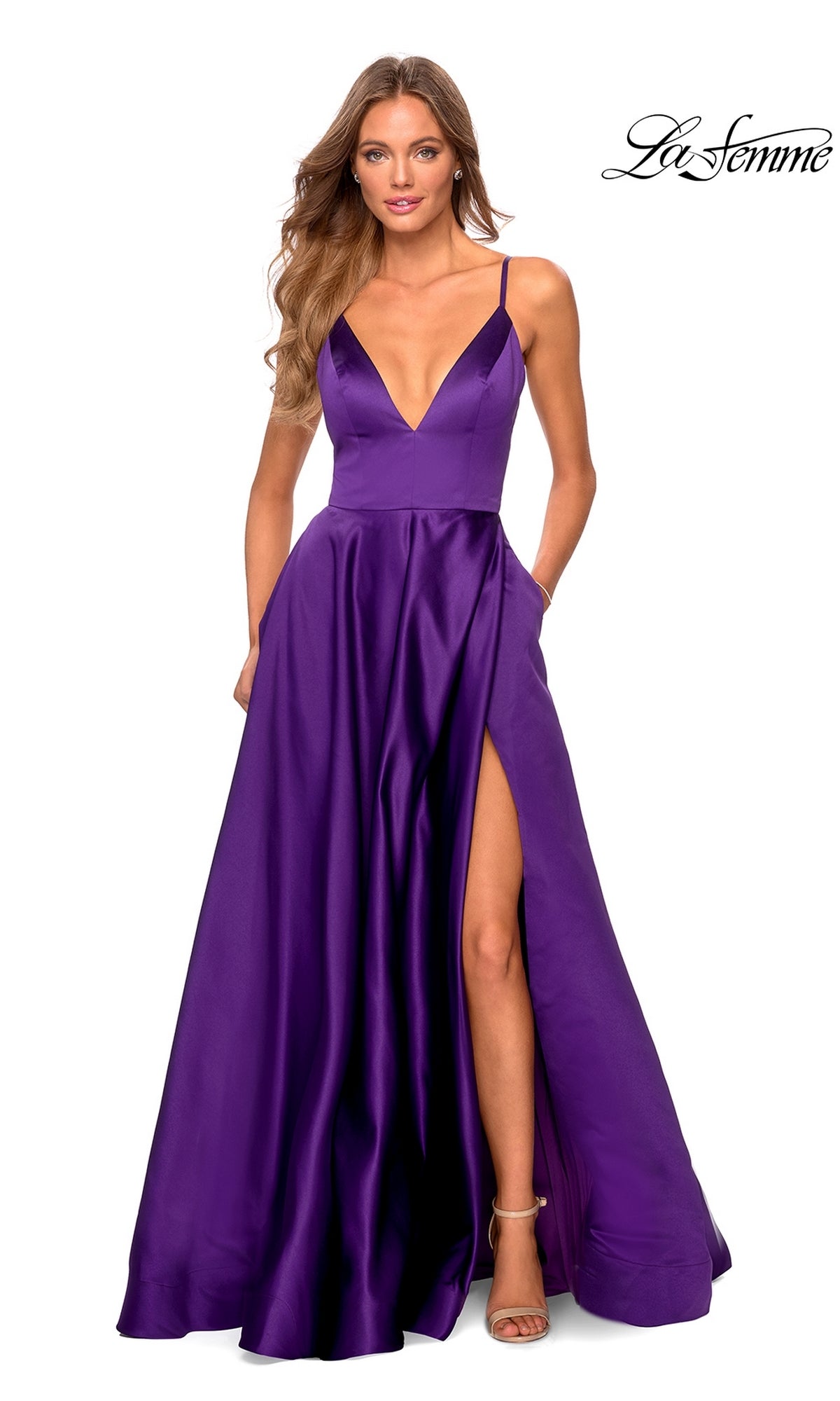 Woman in a La Femme Strappy-Back Long A-Line Prom Dress 28628 in deep purple satin, featuring a deep V-neck, thin straps, high leg slit, and pockets, posing in front of a white background.
