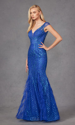 A woman poses against a gray backdrop in the Feathered Cap-Sleeve Long Prom Dress: Juliet 286, a fitted, floor-length royal blue glitter gown with cap sleeves and feather accents.