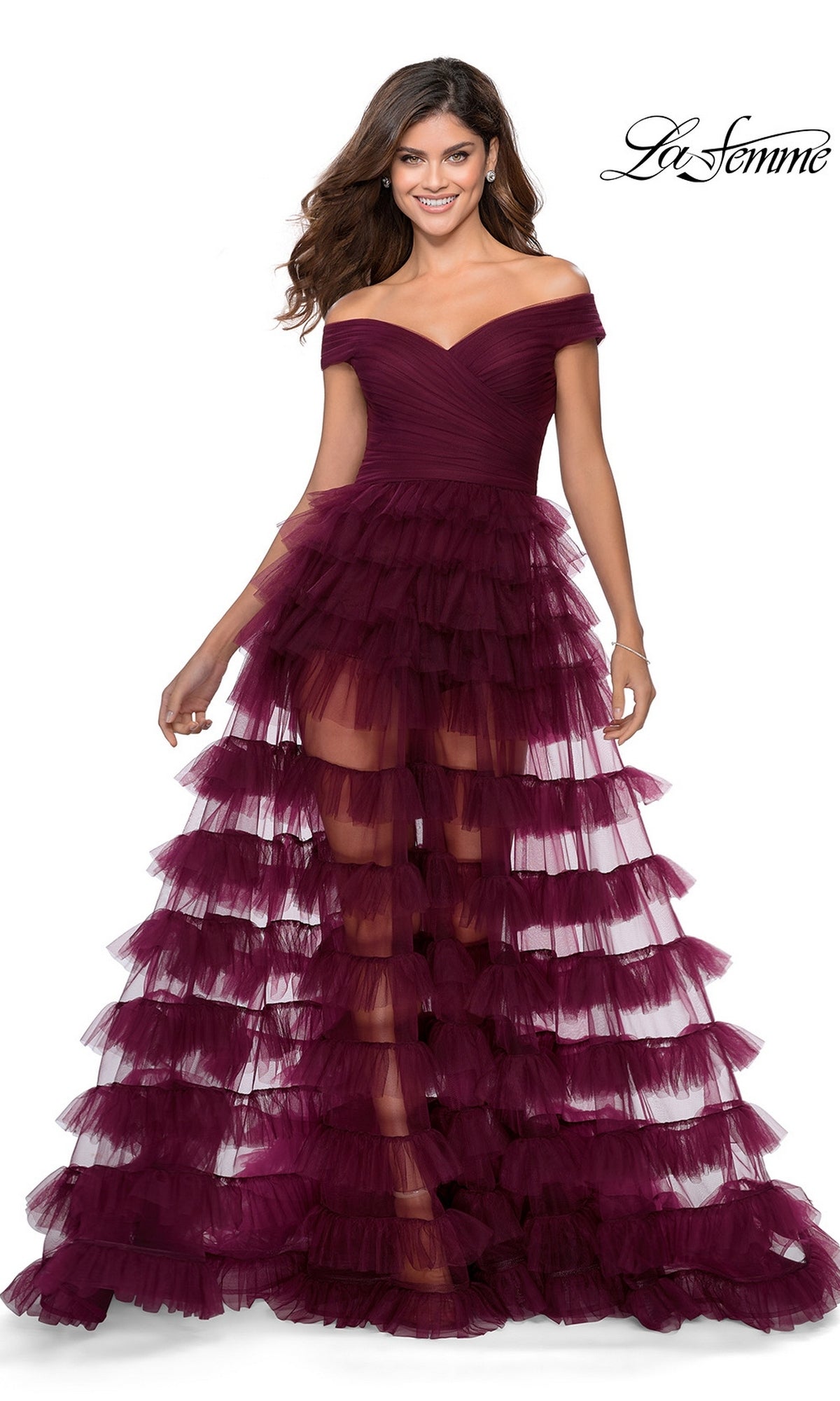 A woman wears a dark berry La Femme 28804 long prom dress featuring an off-the-shoulder design, a ruched bodice, and a tiered tulle skirt.