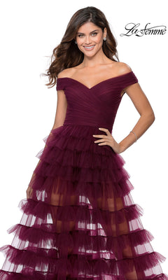 A woman wears a burgundy, off-the-shoulder, tea-length La Femme 28804 prom dress featuring a ruched bodice and a tiered tulle skirt.